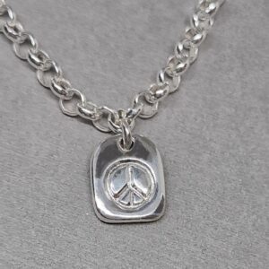Närbild på handgjord fredstag / peace tag i silver på silverarmband. Från Brokig silversmycken.