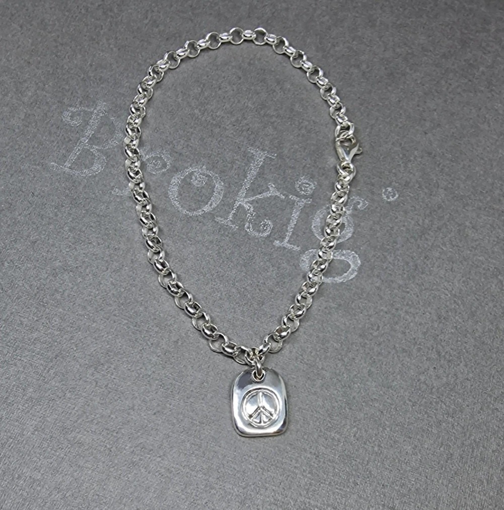 Handgjord fredstag / peace tag i silver på silverarmband. Från Brokig silversmycken.